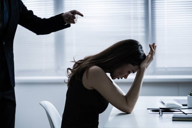 Close-up Of Businessperson Quarreling To Young Businesswoman At Desk